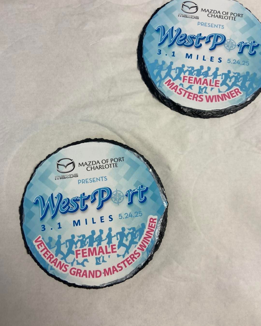 Two blue circular race medals on a white surface, labeled