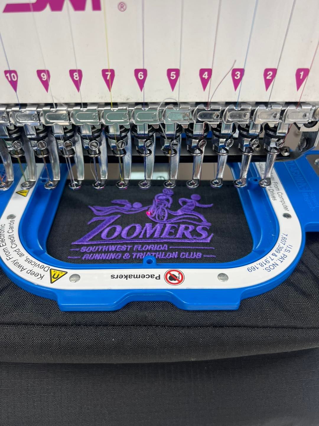 Embroidery machine stitching a blue and black patch with purple text and silver needle heads