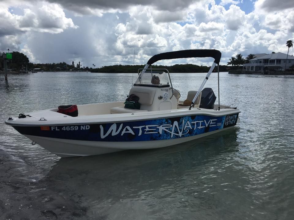 Small blue-and-white boat labeled “WATER NATIVE” floating on calm water under a cloudy sky