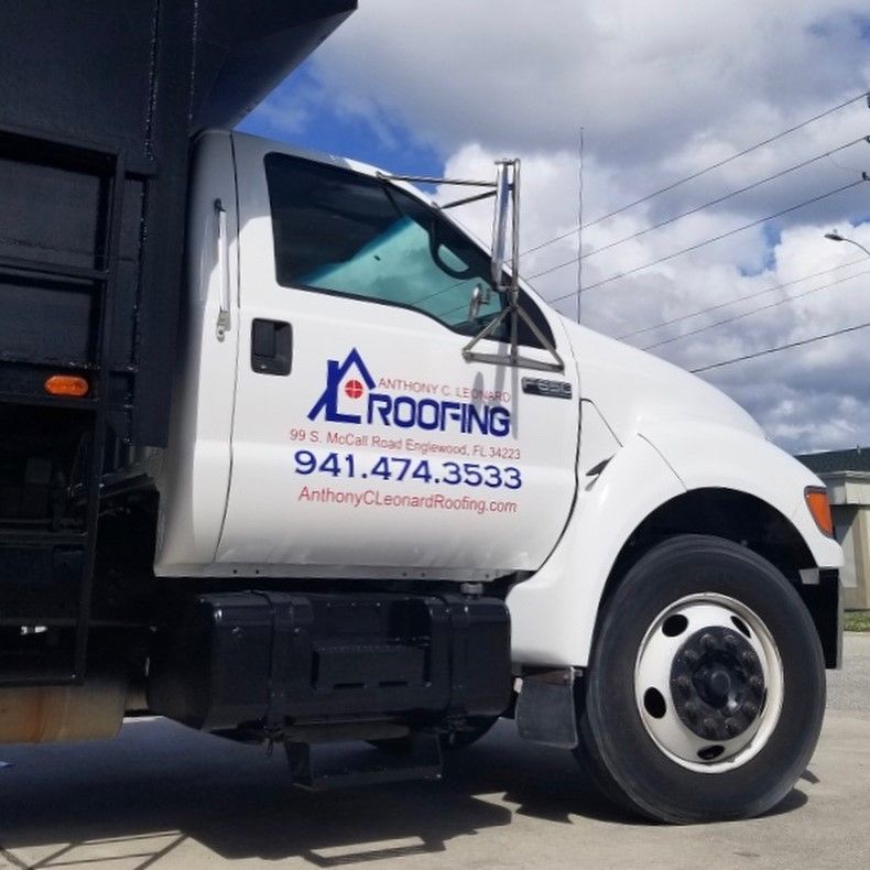 White roofing company truck with logo and phone number parked under a cloudy sky