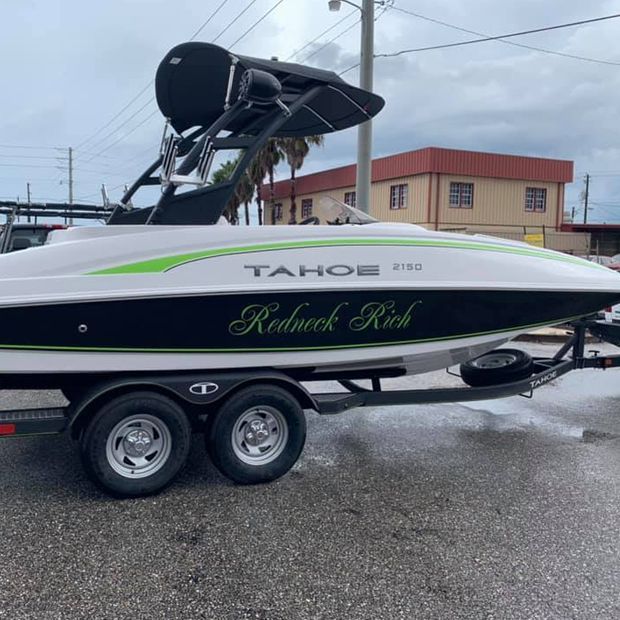 White Tahoe boat on trailer with black canopy and green accents, parked outdoors on wet pavement