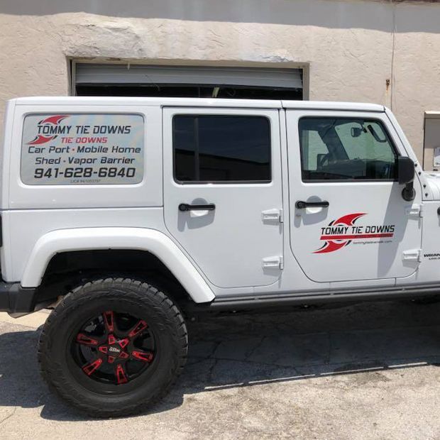 White Jeep Wrangler with “Tuffy Tows” towing service logo parked beside a building
