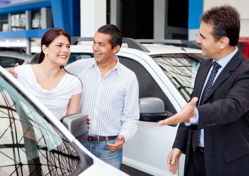 Three people talking beside a white car at a dealership