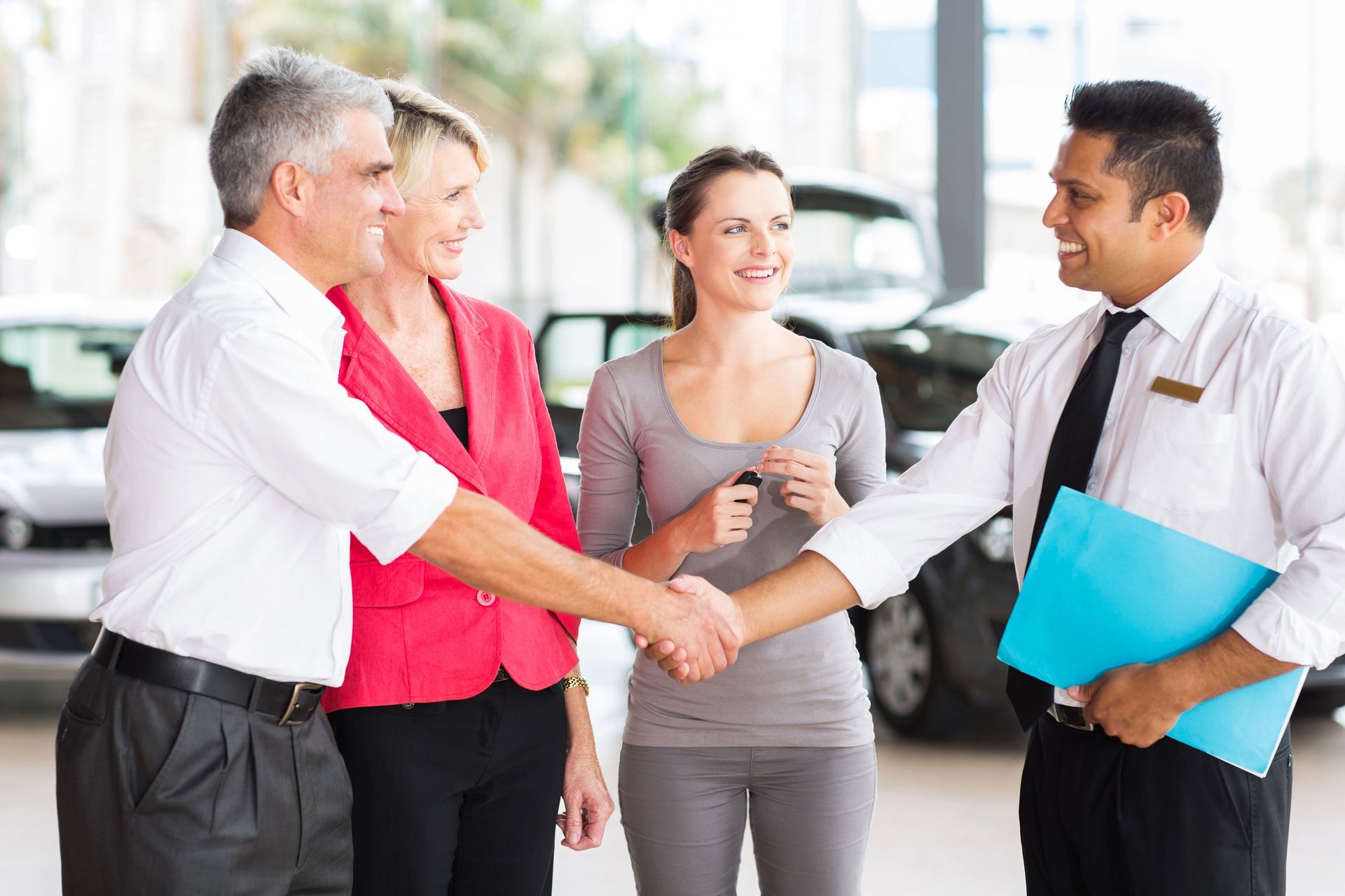 Four professionals shaking hands in a bright office, with a woman smiling in the background.