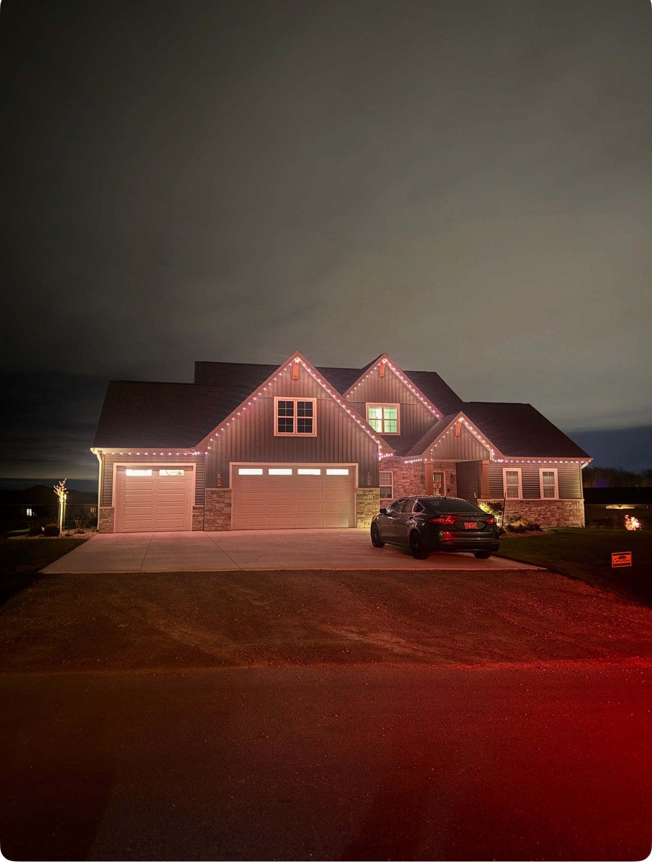 Suburban house at night with garage lights on and a car parked in the driveway