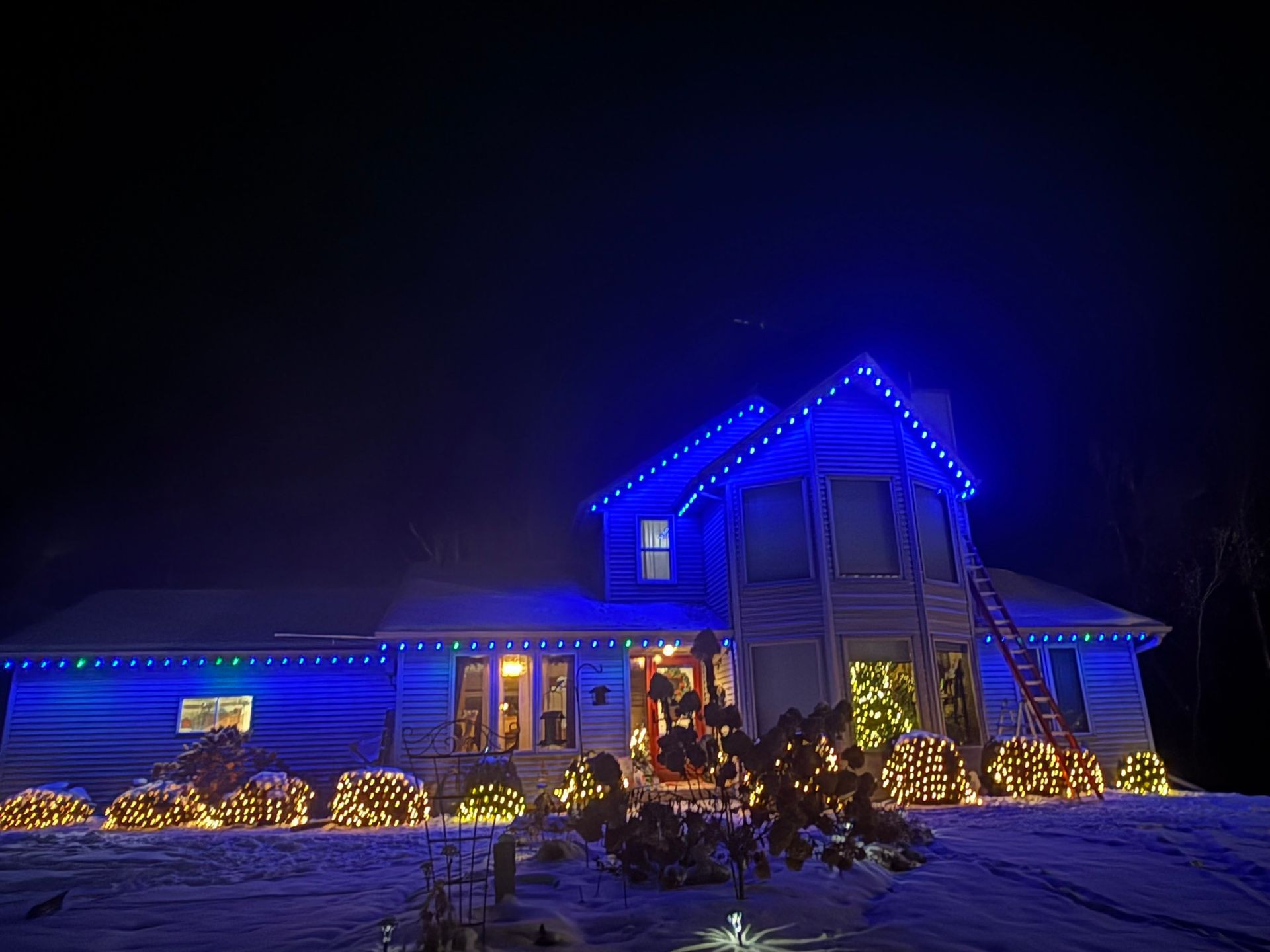 House decorated with bright blue holiday lights and warm glowing yard lights at night