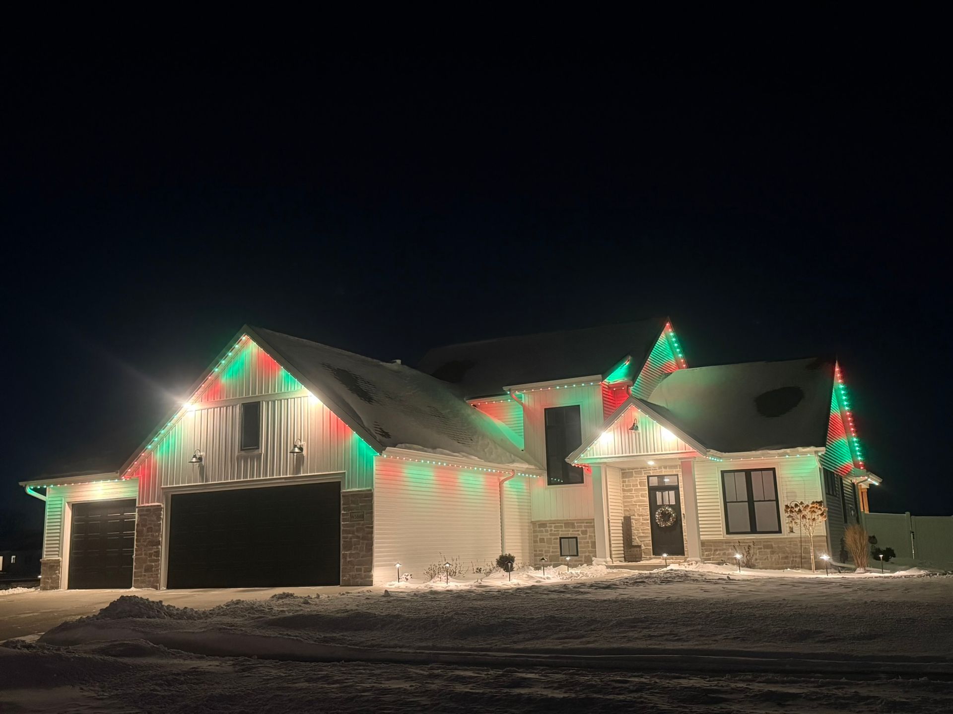 House decorated with red and green holiday lights in a snowy yard at night