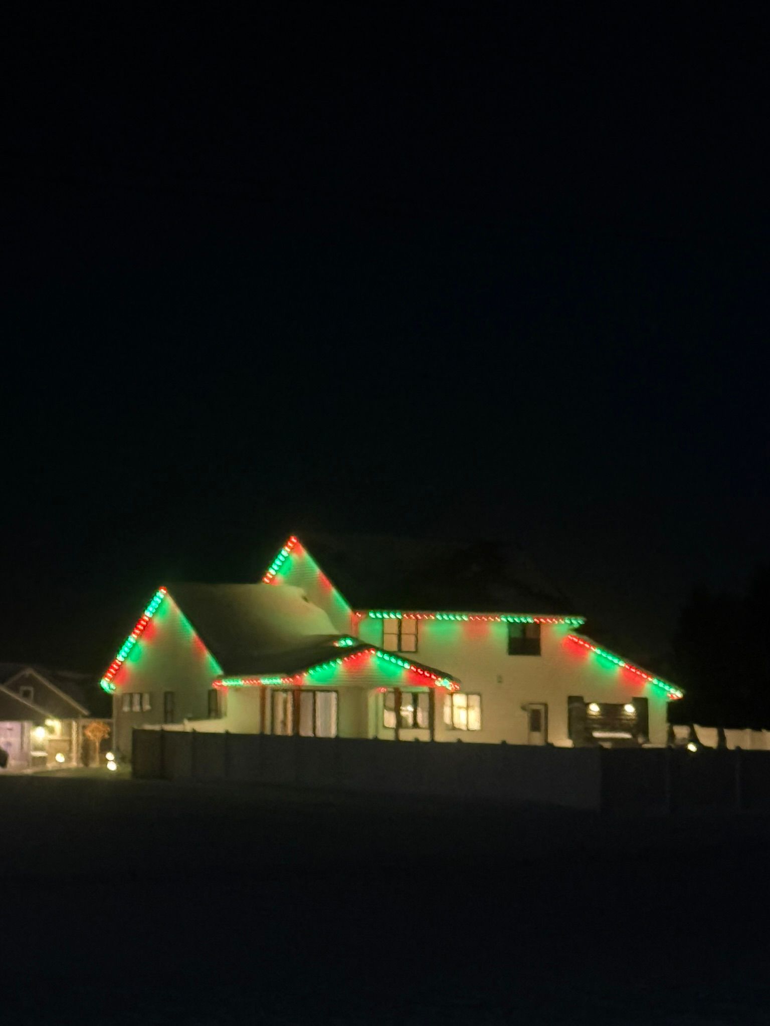 House roofline lit with red and green holiday lights at night
