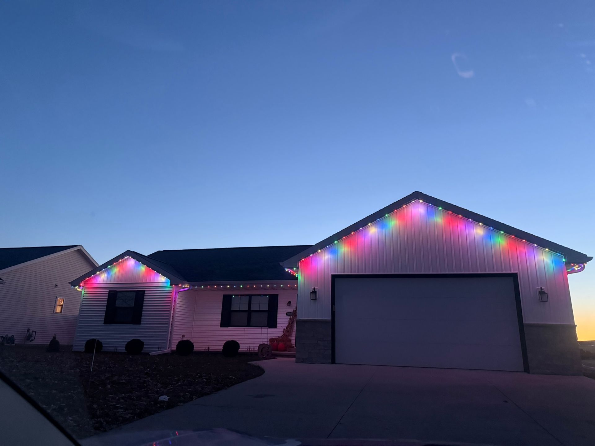 House at dusk with multicolored Christmas lights outlining the roof and garage, garage door closed