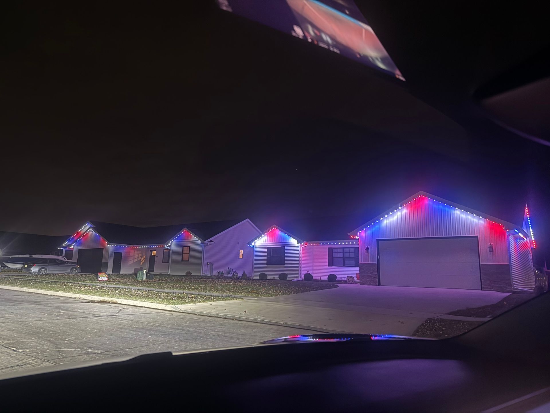 Suburban houses at night outlined with colorful Christmas lights along a snowy driveway