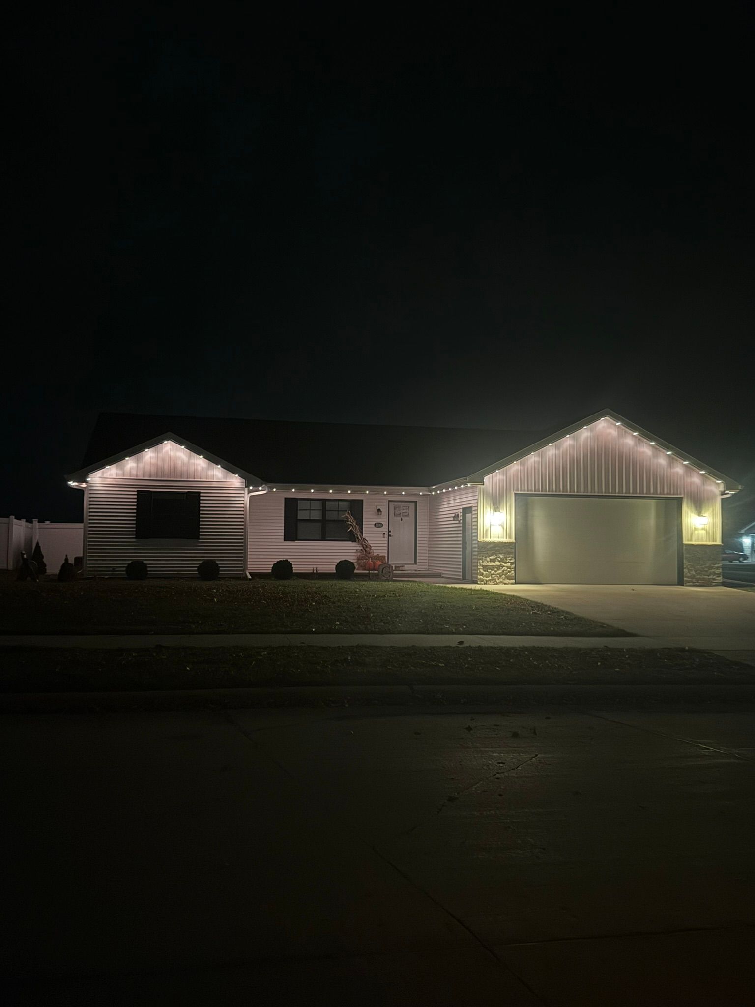 Single-story house at night, outlined with white holiday lights, with a lit garage on the right.