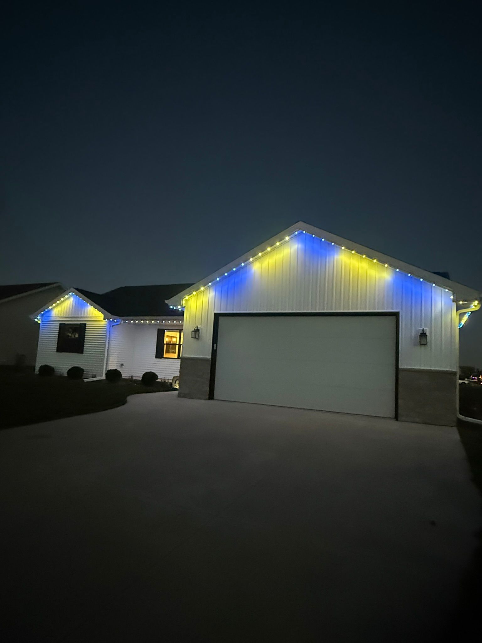 House and garage at night with white and blue holiday lights along the roofline