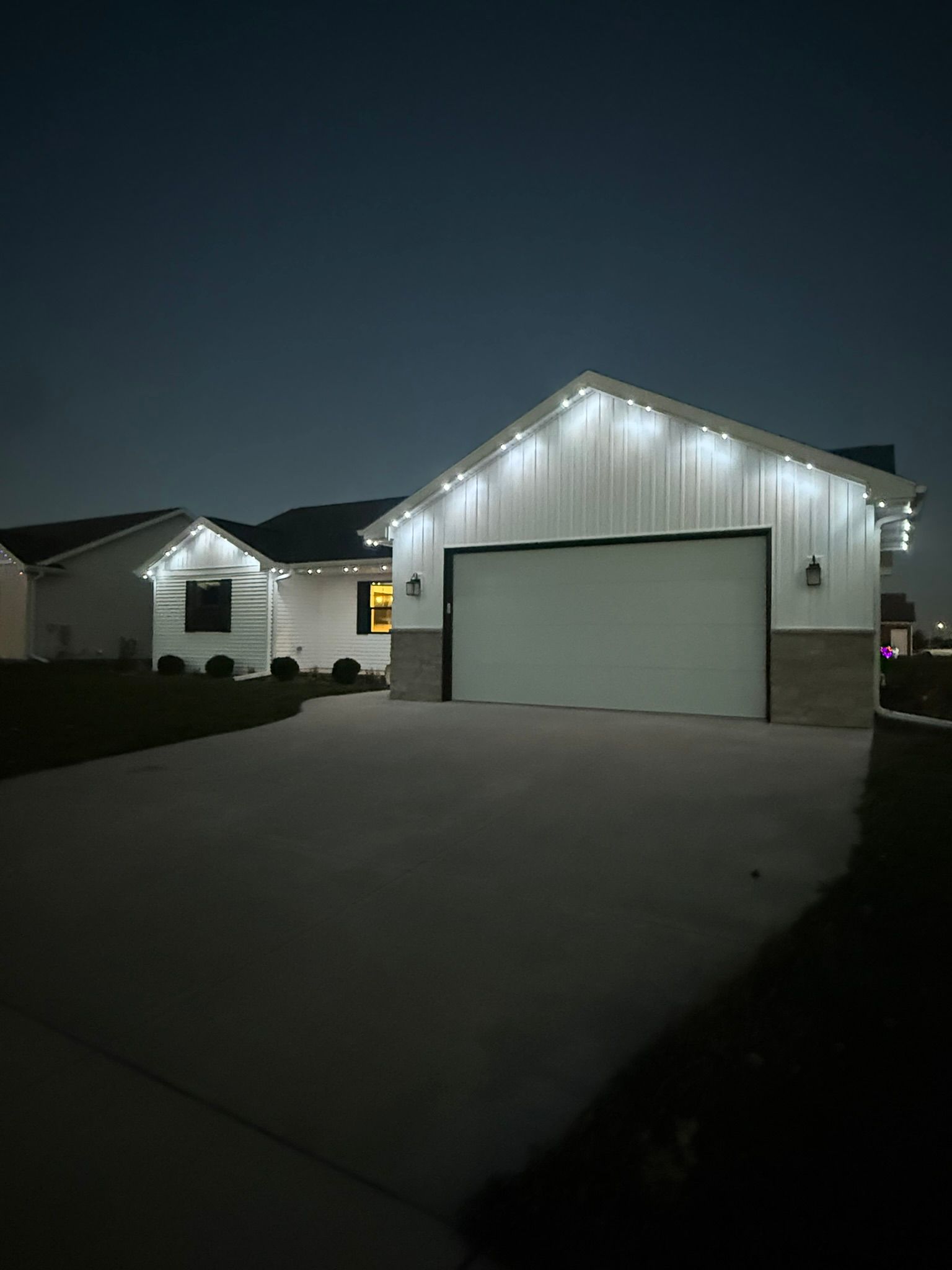 Nighttime suburban house with white garage, lit roofline, and driveway.