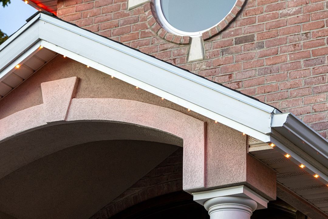 Brick house porch roof with white trim, arched entry, and a round window above the entrance