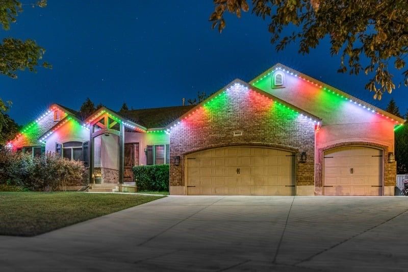 Suburban house and garage outlined with red and green holiday lights at dusk