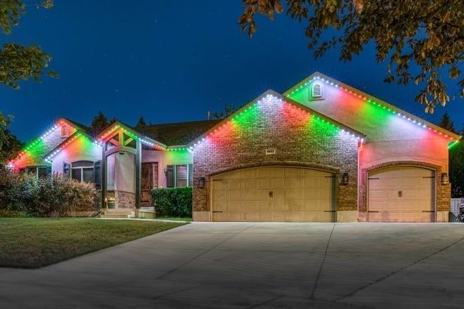 Suburban house and garage outlined with red and green holiday lights at dusk