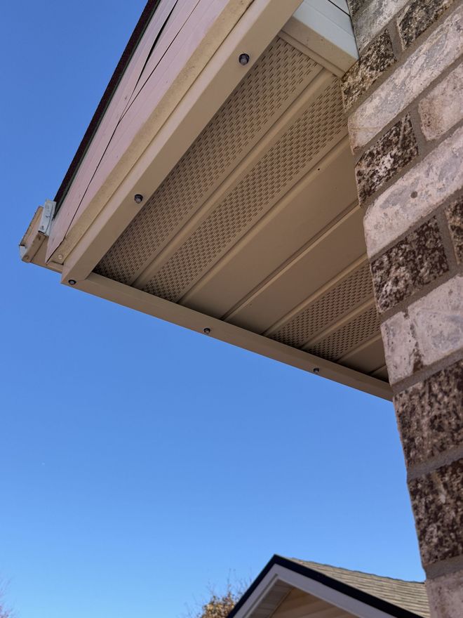 Close-up of a house roof eave with beige soffit vents against a clear blue sky