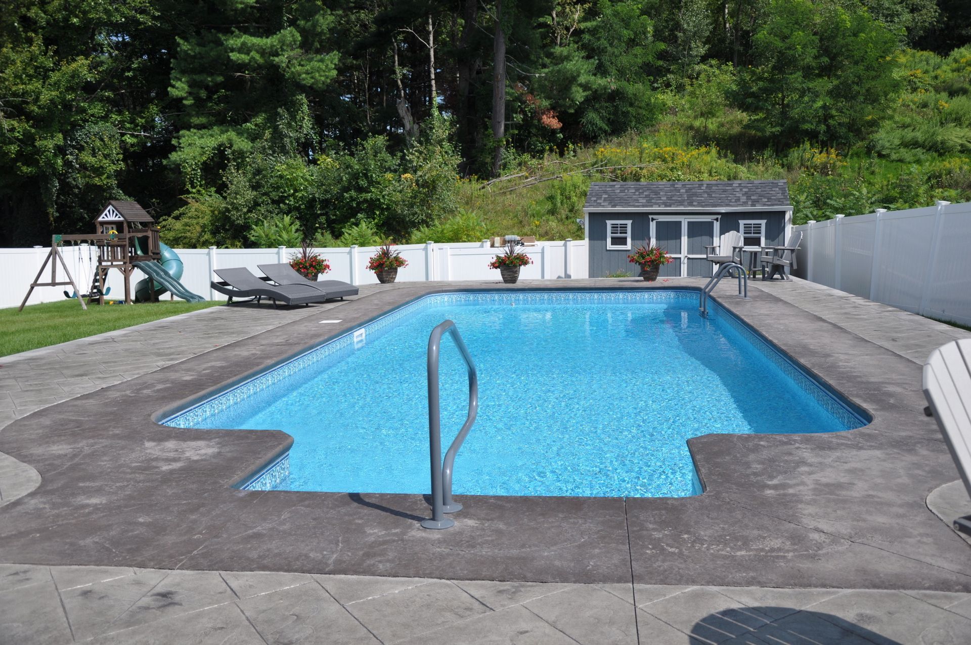 Rectangular swimming pool in a backyard with a shed, playset, and white fence.