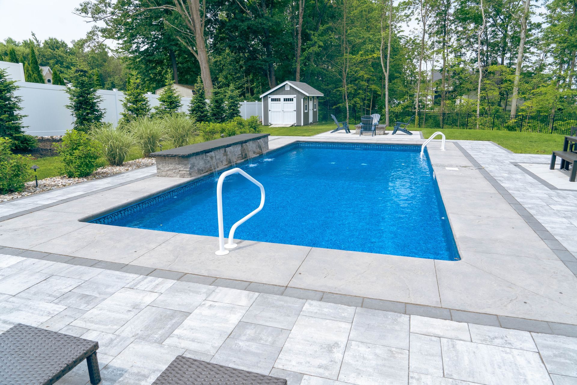 Rectangular swimming pool surrounded by gray stone patio; small shed in the background.