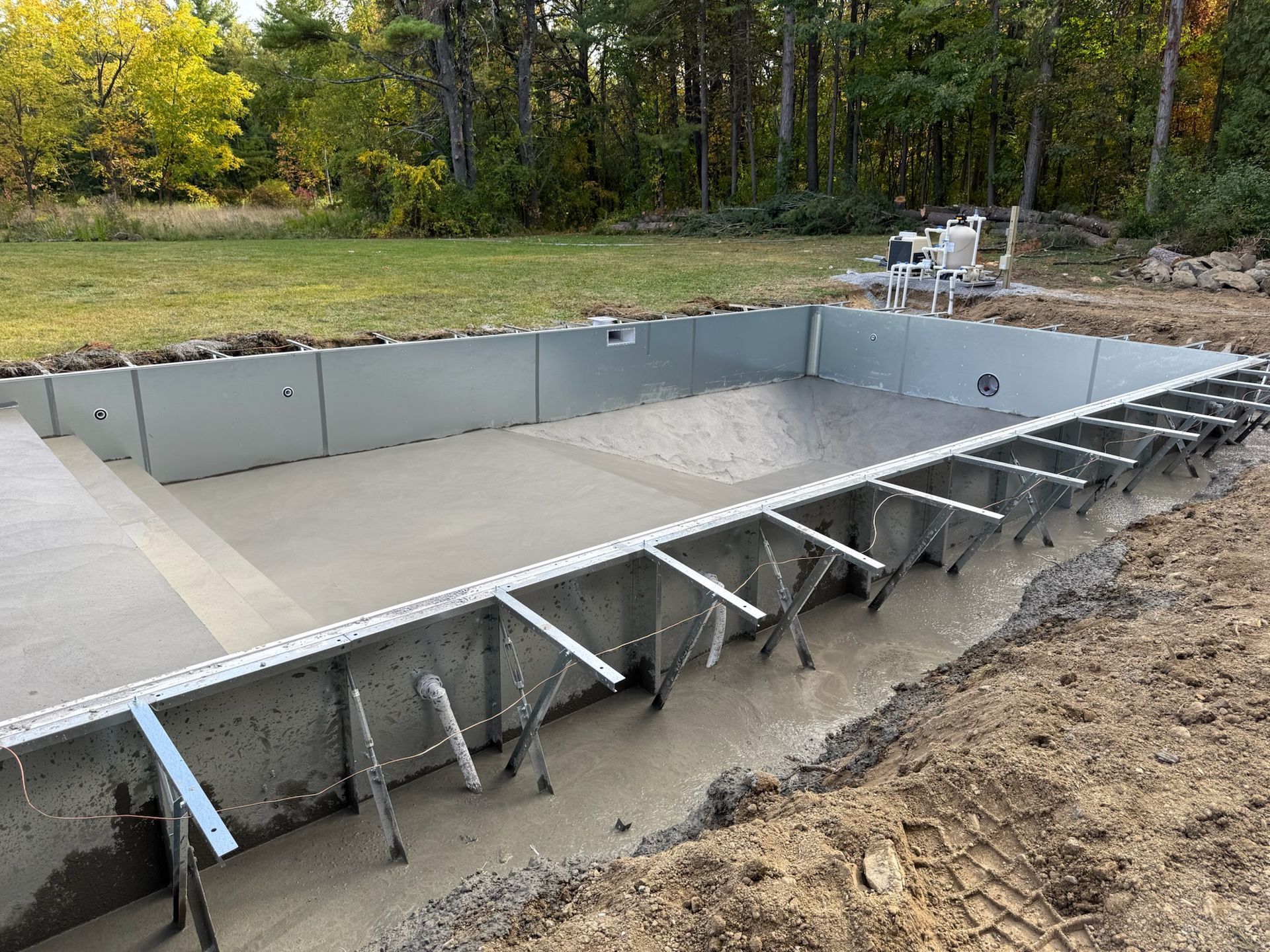 Concrete swimming pool under construction outdoors, with metal supports and surrounding dirt.