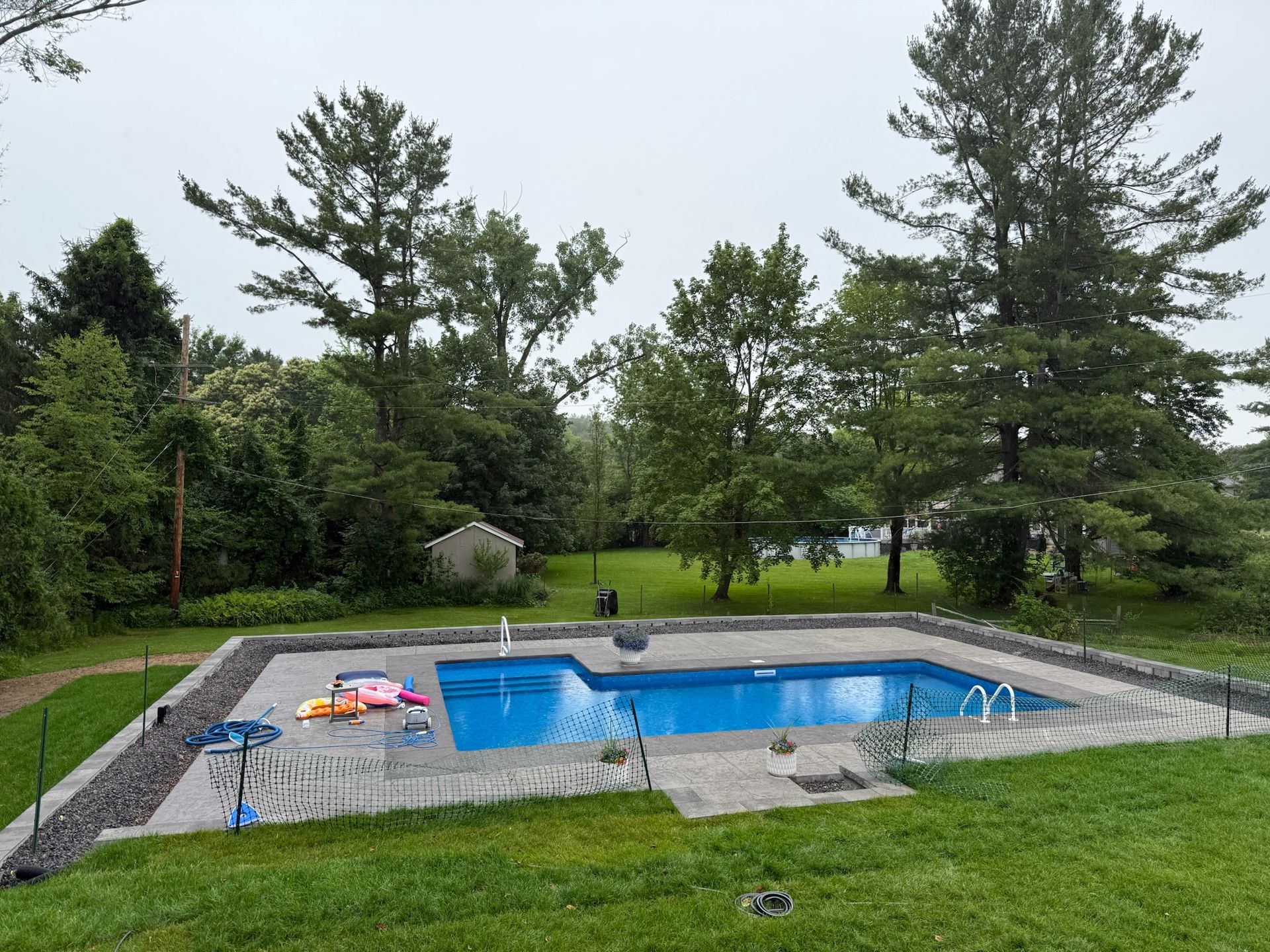 Swimming pool surrounded by green grass and trees on an overcast day.