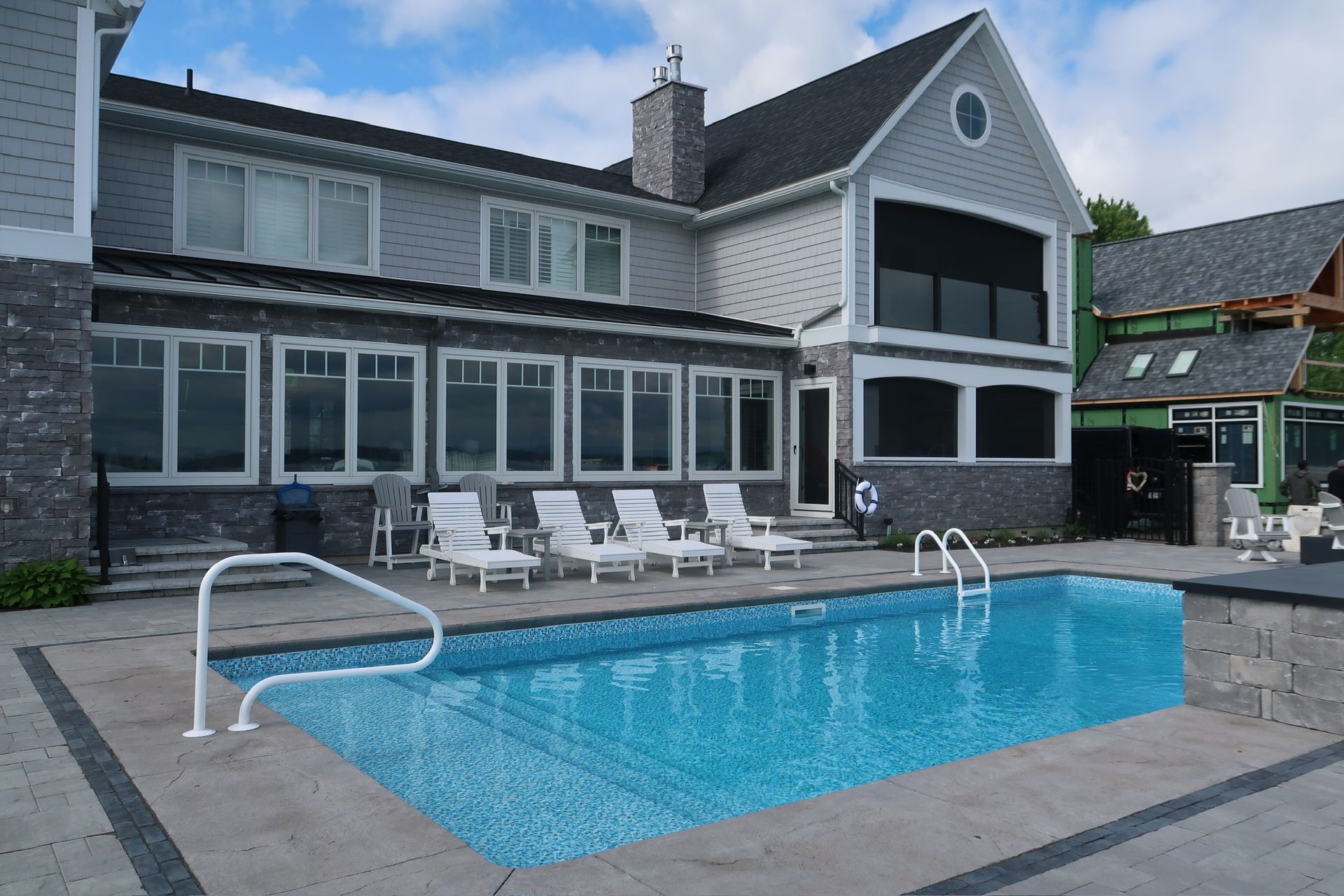 House with swimming pool, lounge chairs, and partial view of a lake under a cloudy sky.