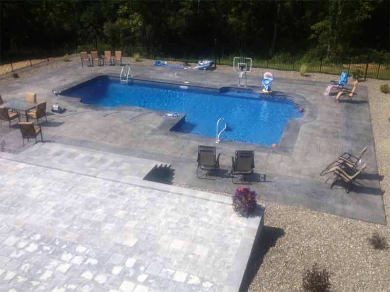 Pool with blue water and gray concrete deck; chairs and basketball hoop.