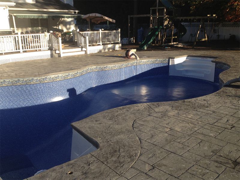 Empty in-ground pool with blue tile and dark gray stamped concrete surrounding it. A person is near the pool.
