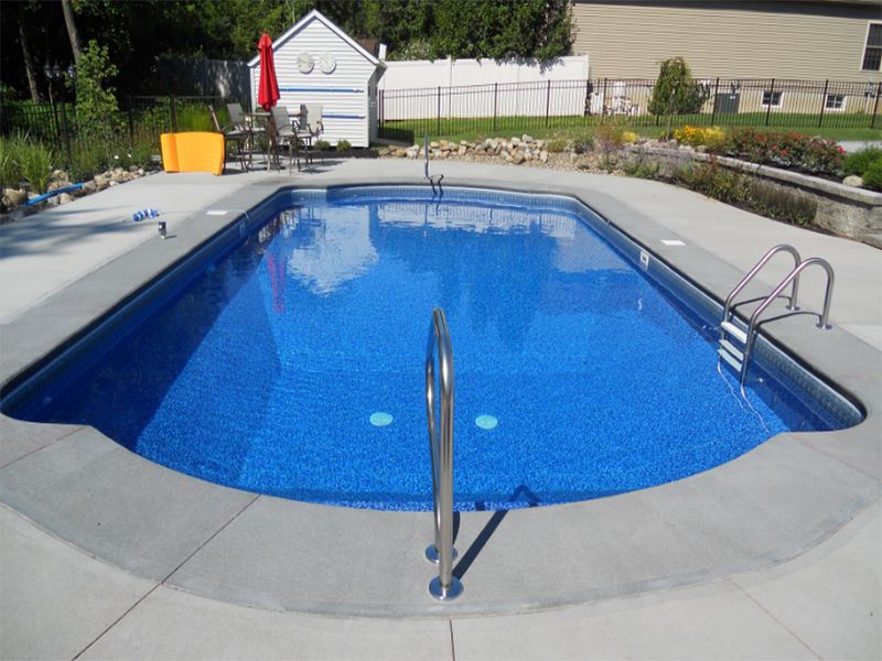 Blue-tiled in-ground swimming pool with gray concrete edging. Stainless steel ladder and handrails.