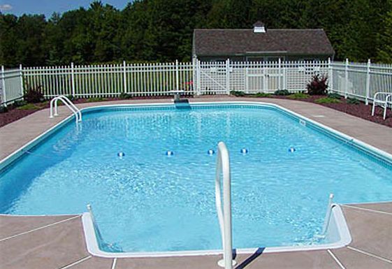 Swimming pool surrounded by a white fence, adjacent to a shed, blue water.