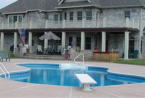 A large brick house with a pool in the foreground. Features include a diving board, patio furniture, and a hot tub.