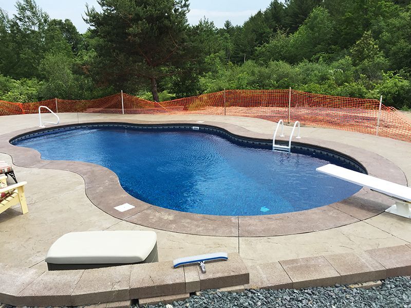 Swimming pool with blue water and concrete deck, diving board. Orange safety fence in the background.