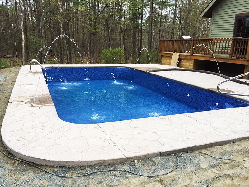 Rectangular swimming pool with blue tile interior, water fountains, and concrete border, near a deck.
