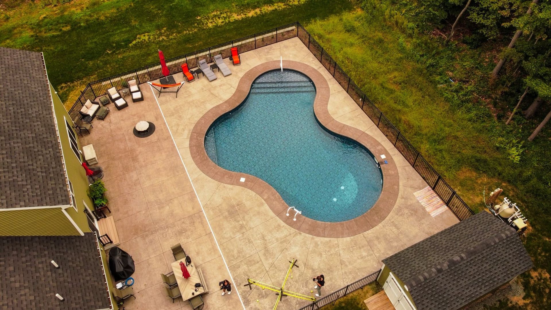 Aerial view of a swimming pool with a surrounding patio, lounge chairs, and a small building.