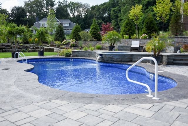 Blue-tiled, kidney-shaped pool with a water feature, surrounded by gray paving stones and landscaping.