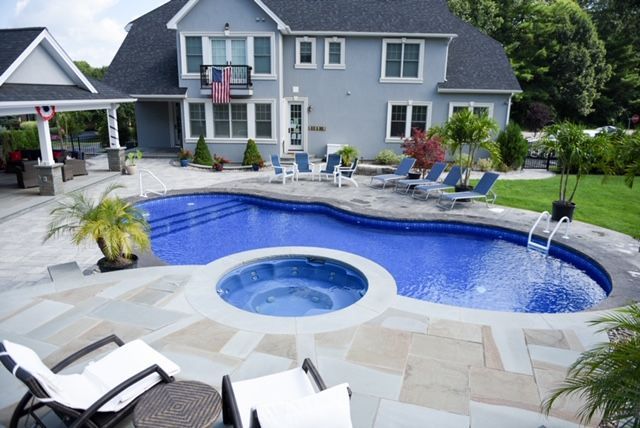 Backyard pool with spa, blue water, stone patio, lounge chairs, and two-story gray house.