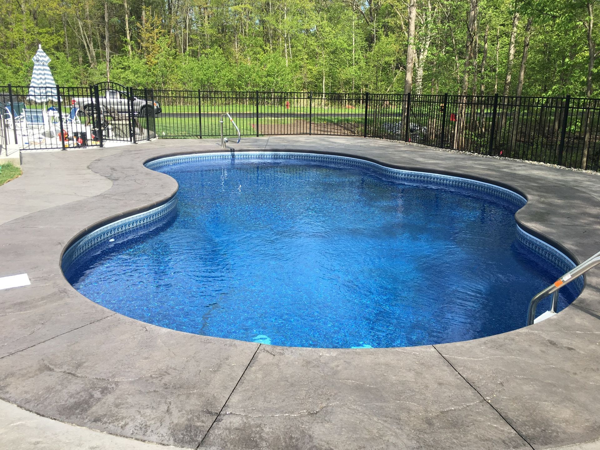 A kidney-shaped pool with blue water surrounded by a gray concrete patio and black fence.