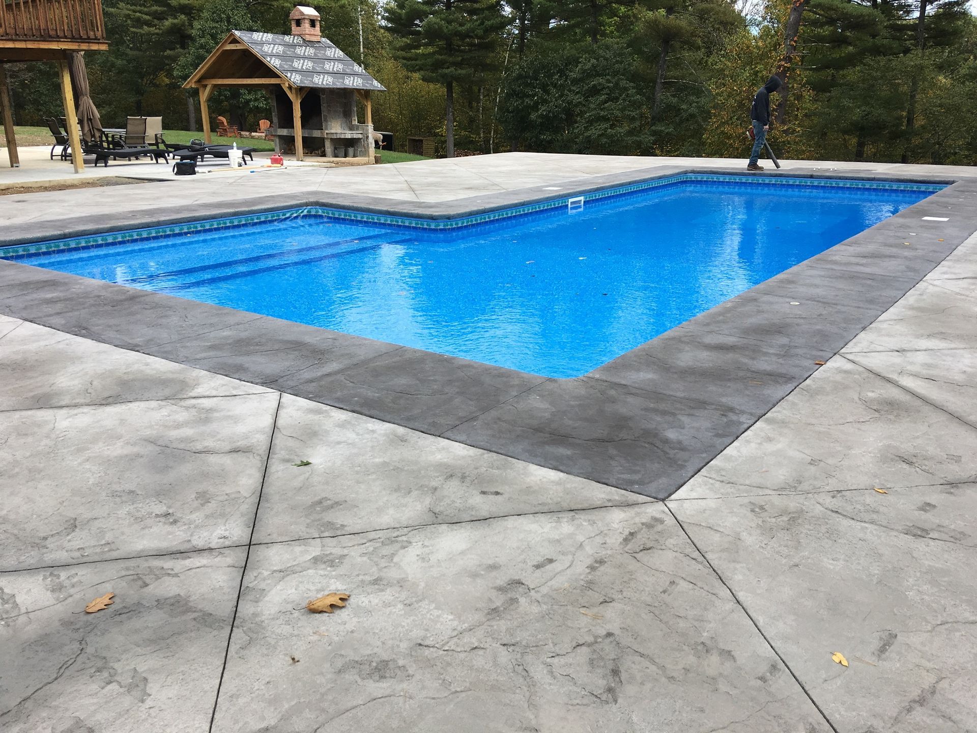 Rectangular in-ground pool with blue water and gray concrete deck. A person stands nearby.