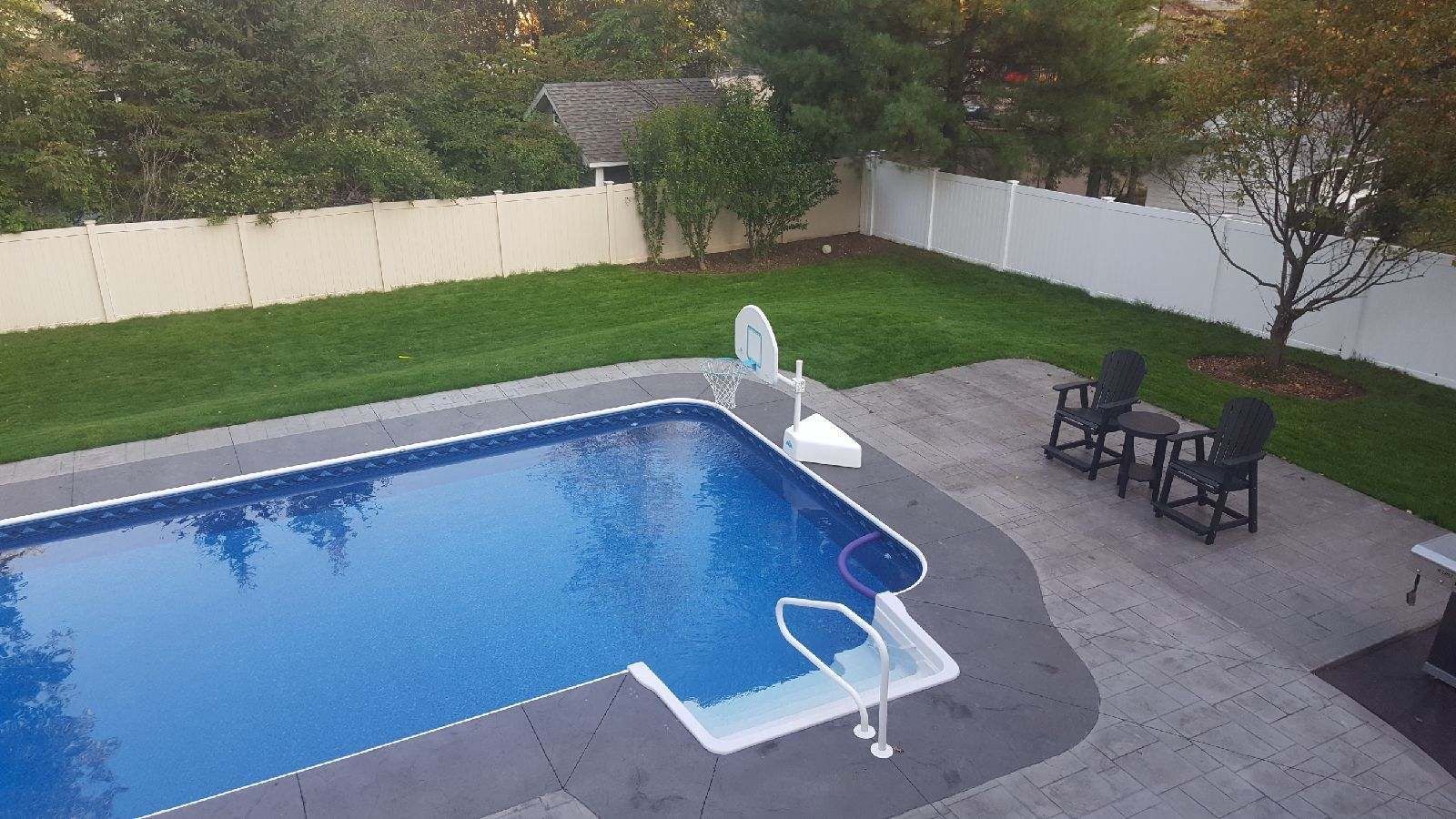 Backyard pool with patio, lawn, and white fence; two chairs sit on the patio.