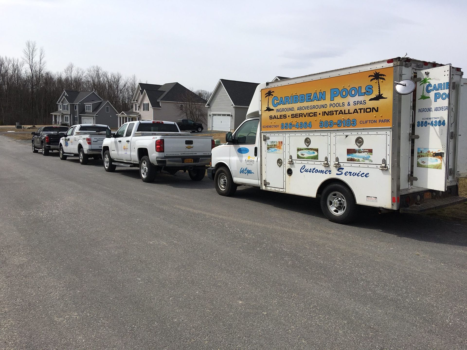 White service van and trucks parked on a street. The van has 