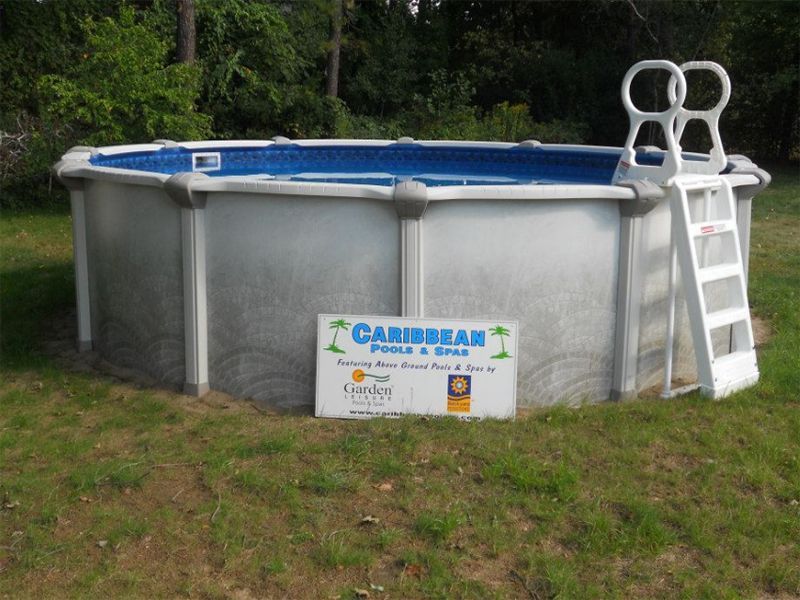 Above-ground, octagonal pool with ladder, on grass. The pool's side has a sign for Caribbean Pools & Spas.