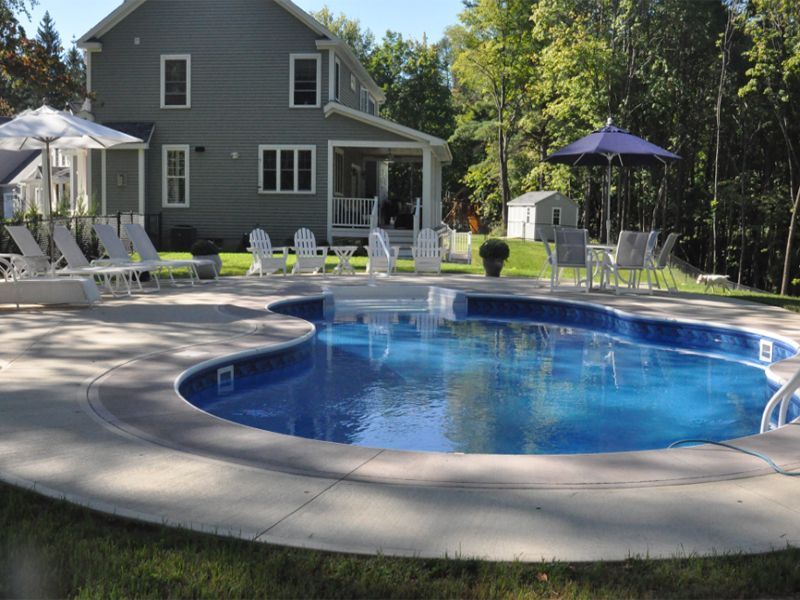 Backyard pool with surrounding patio, chairs, and house with a green exterior.