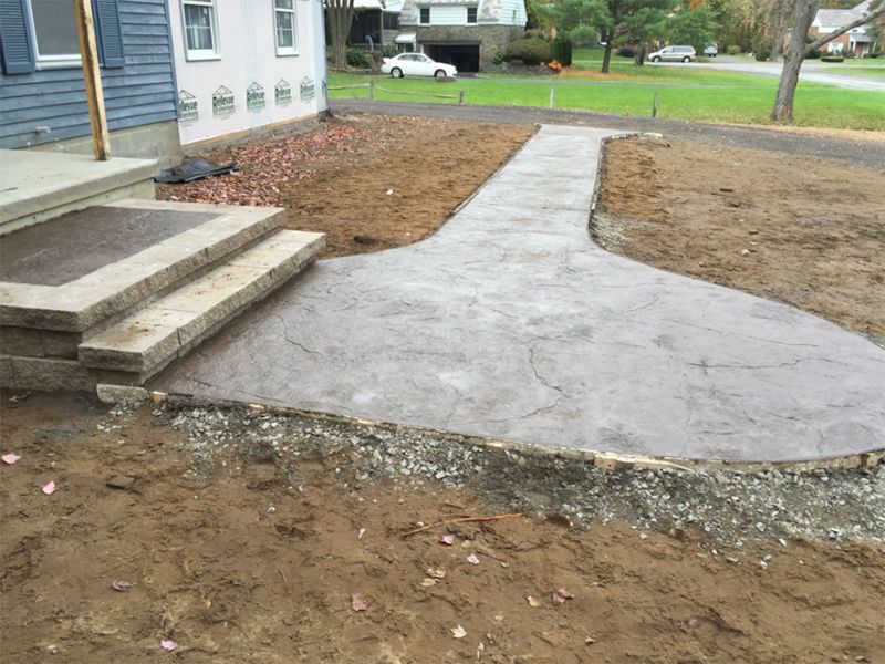 Concrete pathway leading from house steps to a driveway, set in bare earth.