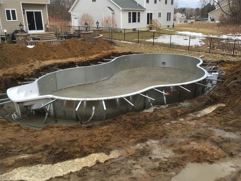 Partially constructed in-ground pool, steel frame, concrete base, surrounded by mud.