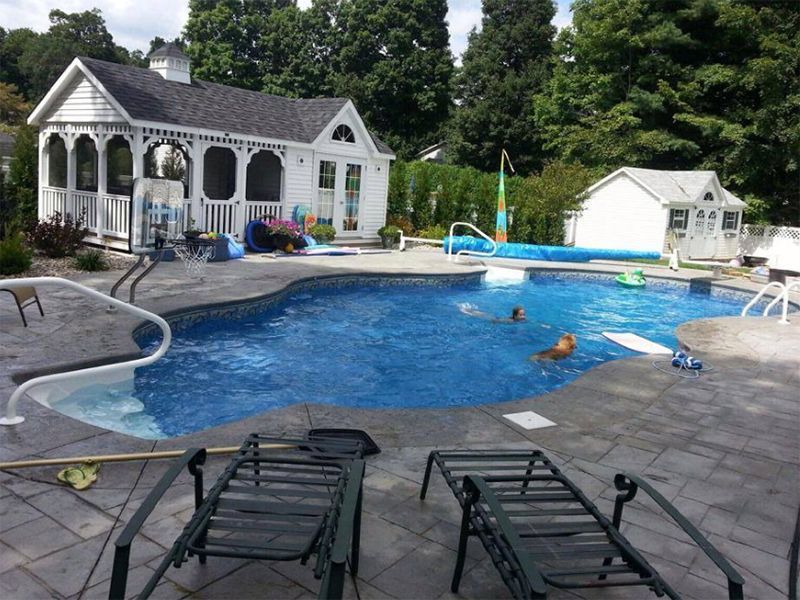 Pool in backyard with gazebo, shed, and two people swimming. Loungers in foreground.
