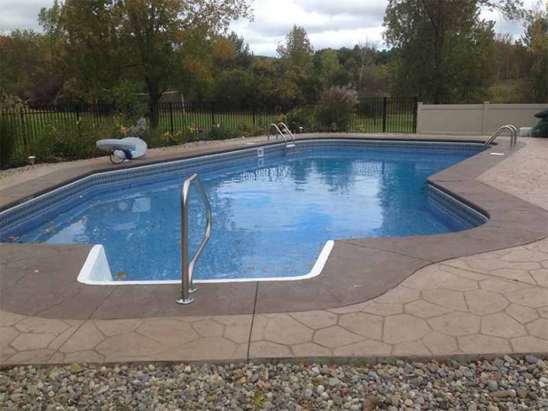 Swimming pool with blue water and gray concrete edging, surrounded by landscaping and fence.
