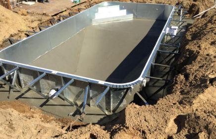 Pool under construction in a dirt pit; concrete bottom and steel frame.
