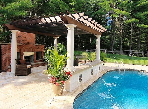 Pergola with pillars over a pool, outdoor fireplace, and greenery.