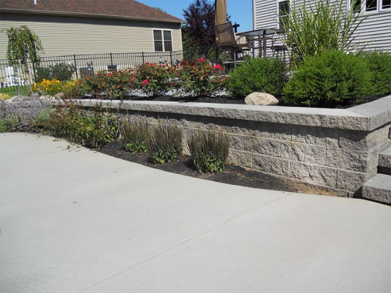 Stone retaining wall with a garden bed of flowers and shrubs in a backyard.