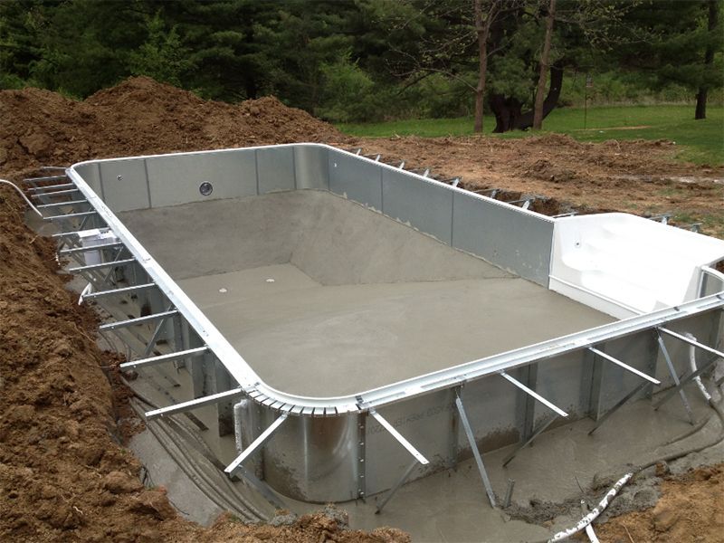 Pool under construction: rectangular metal frame in a dirt excavation, with concrete base.